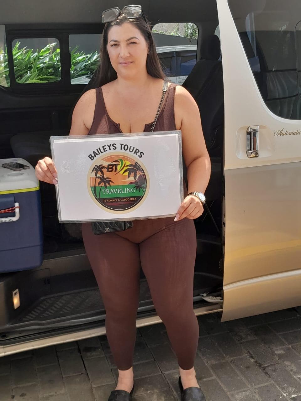 Guest holding a Baileys Tours sign beside the tour van